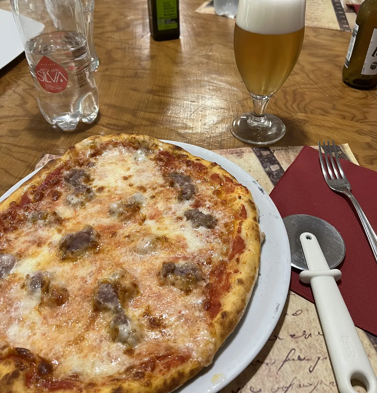 Pizza con salsiccia e una birra alla spina sul tavolo